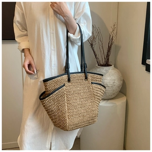 Detail of a woven straw tote bag with black leather straps and side pocket for beach trips