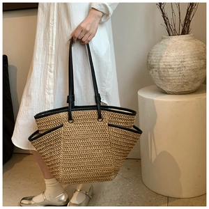 Detail of woven straw tote bag featuring black leather trim and functional side pockets