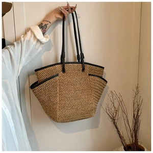Detail of a large straw tote bag with black leather straps and side pocket for travel