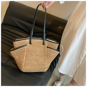Detail of large straw tote bag with black leather trim and handles on a black seat
