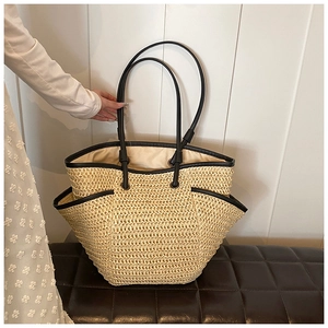 Detail of hand-woven straw tote with black leather straps and side pockets on bench