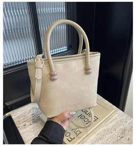 Détail du sac cabas tissé beige avec poignée ronde et bandoulière amovible sur marbre