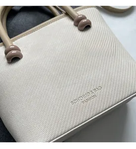 Gros plan du sac à main en tissu texturé crème avec logo embossé et poignée contrastée