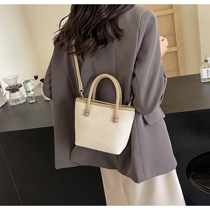 Détail du sac trapèze beige montrant le cuir texturé et les poignées rondes brunes