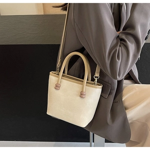 Détail du sac cabas crème avec perles sur l'anse et logo sur un costume gris minimaliste