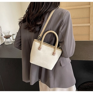 Détail du sac beige à texture litchi avec poignée cylindrique et crochet en métal