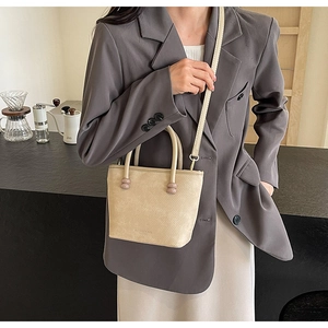 Sac seau beige minimaliste avec perles mauves porté sur l'épaule sur un blazer gris