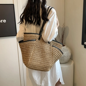 Straw woven tote bag with black leather straps shown on model for seaside beach vacation