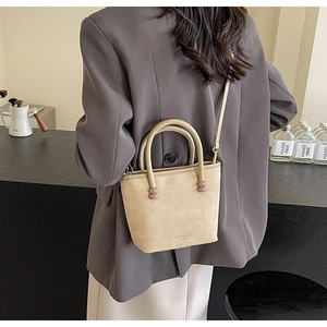 Détail du sac seau beige avec texture croisée et perles décoratives sur l'anse