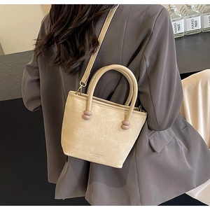Détail d'un sac trapèze beige minimaliste avec poignée à perles sur fond de costume gris