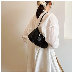 Detail of a black crescent moon shoulder bag with silver buckle worn by a model