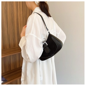 Minimalist black leather crescent bag with silver buckle worn on shoulder by a model
