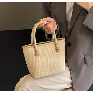 Détail du sac cabas beige texturé avec perles marron tenu par un mannequin