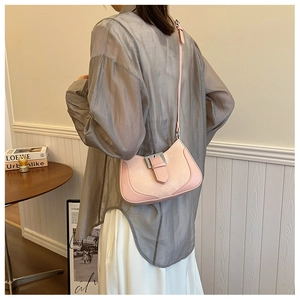 Detail of light pink hobo bag with silver buckle worn on shoulder in home setting