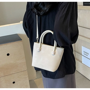 Sac bandoulière beige chic avec poignées anneaux et cuir texturé sur un mannequin