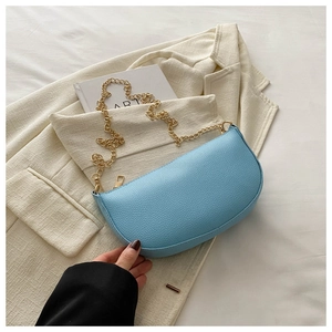 Detailed macro view of light blue saddle bag featuring pebble texture and gold chain strap