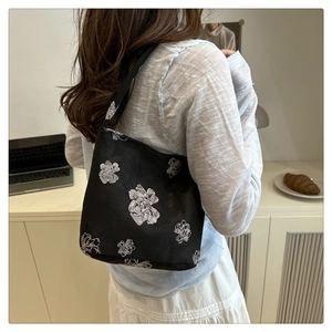 Detail of black fabric tote bag featuring white floral patterns and slim shoulder straps