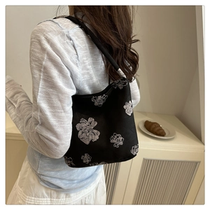 Detail view of a black canvas tote bag with white flower print on a female model