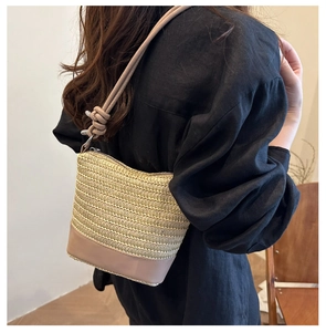 Detail of a beige woven straw crossbody bag with pink leather trim and knotted strap