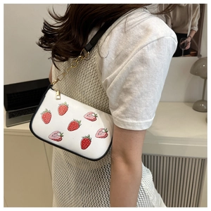 Détail d'un sac à bandoulière blanc avec imprimé fraises et chaîne en métal doré