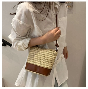 Detail of hand-woven straw bucket bag with dark brown leather base and slim shoulder strap