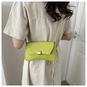 Avocado green leather baguette bag with gold buckle shown on a model in a minimal setting