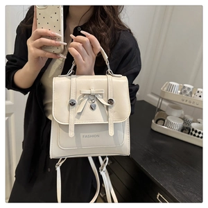 Close-up of cream white handbag with decorative bow and silver heart pendant detail