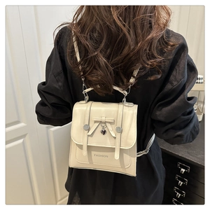 Detail of cream mini backpack featuring a bow accent and heart charm shown on a model