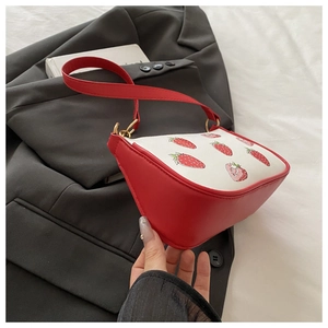 Detail of red and white strawberry print shoulder bag on a black blazer background
