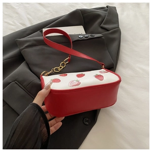Detail of red strawberry print handbag featuring gold metal chain links on a leather strap
