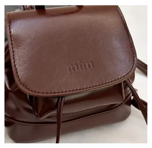 Detailed view of glossy dark brown leather backpack featuring drawstring and mim logo