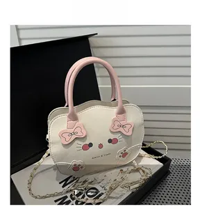 Detalle del estampado de gato en bolso crema con lazo rosa y correa de cadena dorada