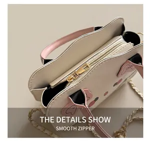 Detalle de la cremallera dorada y asa rosa en el bolso bandolera blanco con gato