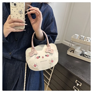 Detalle de bolso bandolera blanco con forma de gato, lazo rosa y correa de cadena