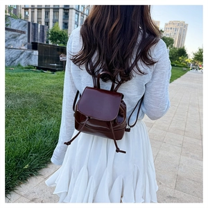 Outdoor shot of a deep wine red mini backpack with glossy finish and drawstring detail