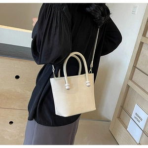 Détail d'un sac bandoulière crème avec texture sergé et accents perlés sur les poignées