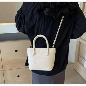 Détail d'un sac bandoulière beige texturé avec poignées cylindriques et fine bandoulière