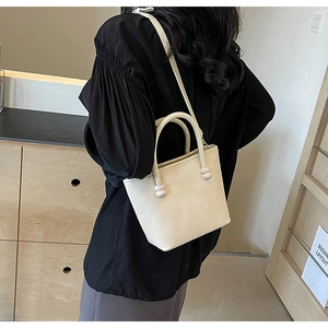 Détail du sac crème texturé avec poignée ornée d'une boule et bandoulière amovible