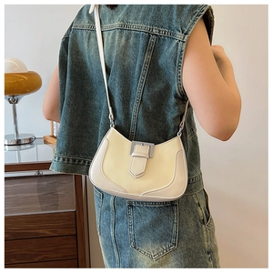 Detail of cream saddle bag with metal buckle worn by model in a denim vest