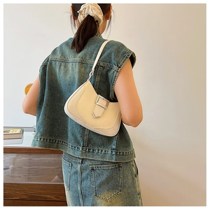 Detail of a minimalist off-white crescent underarm bag with silver buckle on a shoulder