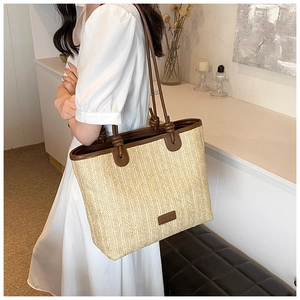 Close-up of a large straw tote bag with brown leather handles and detail on front logo