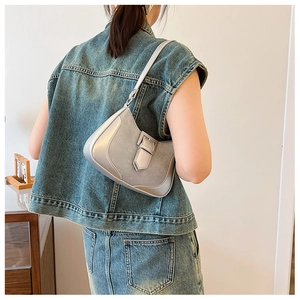 Silver metallic shoulder bag with wide metal buckle shown on model in indoor setting