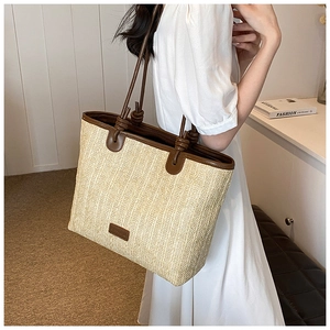 Detail of hand-woven straw tote bag with brown leather shoulder straps and knot design