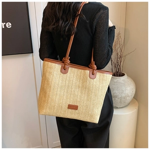 Detail of hand-woven straw tote bag featuring brown PU leather straps and knotted accents