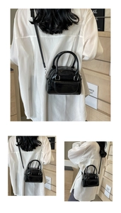 Detail of a black shiny shell bag with adjustable shoulder strap and top handles