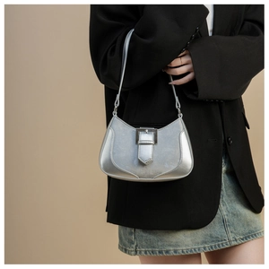 Detail of silver metallic crescent underarm bag with decorative buckle on model