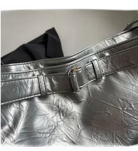 Detailed close-up of wrinkled silver metallic fabric and bronze buckle on shoulder bag