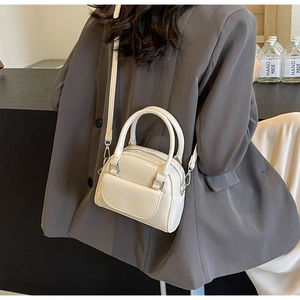 Detail einer cremeweißen Boston-Tasche aus glänzendem Leder getragen zum grauen Blazer