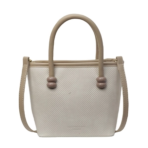 Sac à main beige texturé avec bordure kaki et perles décoratives sur fond blanc
