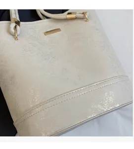 Dettaglio della borsa a secchiello bianco perla con pelle testurizzata e finiture dorate